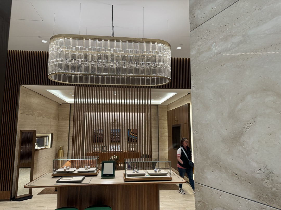 Rolex luxury showroom with crystal chandelier, wood slat partitions, and precision display case lighting — electrical installation by Burlingame Brothers Electric