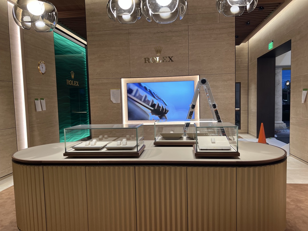 Rolex showroom counter with glass display cases, backlit video wall, chrome globe pendant lights, and green wave accent wall — electrical by Burlingame Brothers Electric
