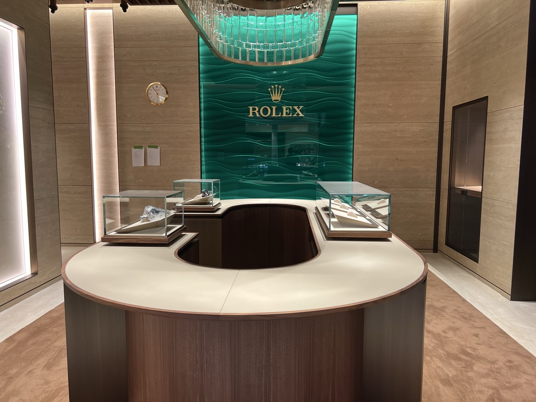 Rolex signature green wave wall with gold crown logo, custom crystal chandelier, and illuminated glass display cases — lighting by BBE Electric
